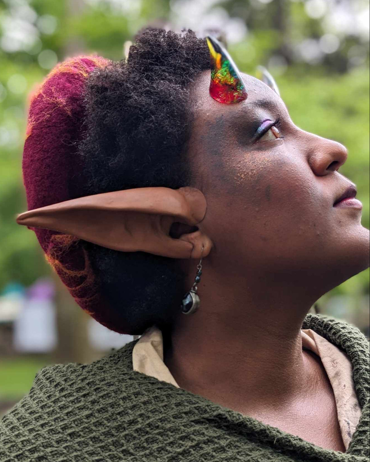 A person wearing a green outfit with fantasy-style elf ears prosthetics and glue on resin horns