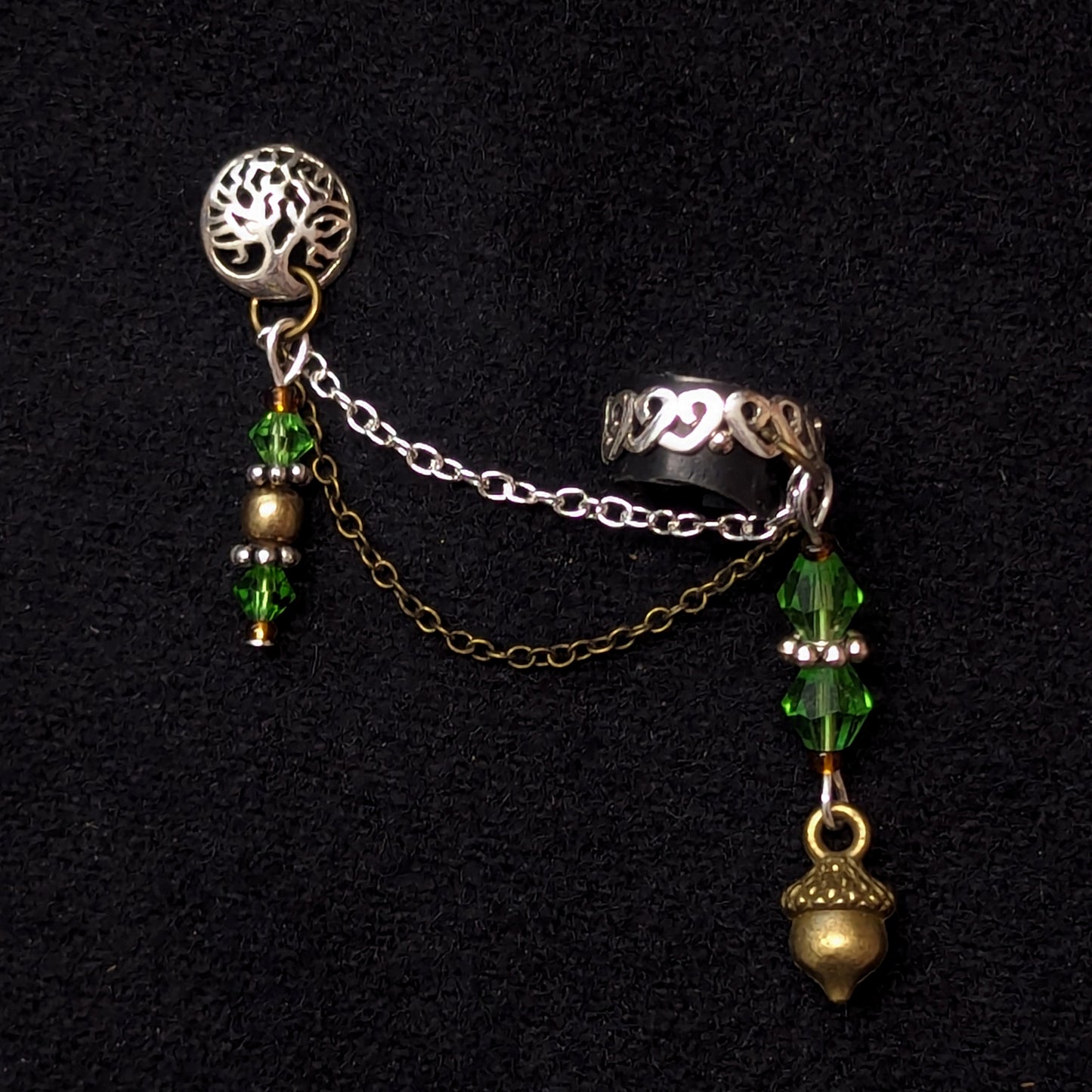 A sterling silver ear cuff with a tree of life design on the post and a brass acorn drop with amber and light green beads on the cuff.