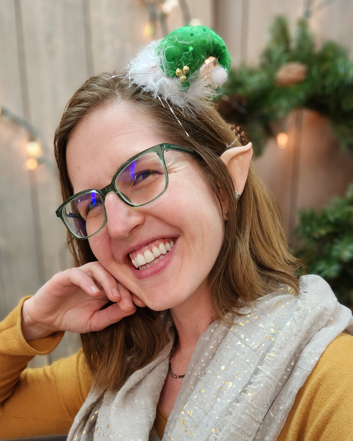 A person smiling and wearing elf ears with a holiday hat.