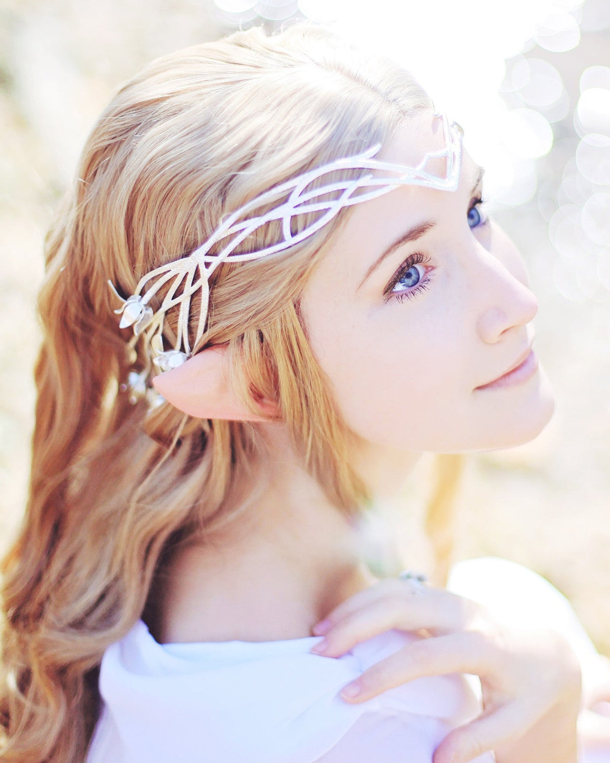 A person with blonde hair wearing white Wood elf ears prosthetics, designed to be attached to the head for a costume.