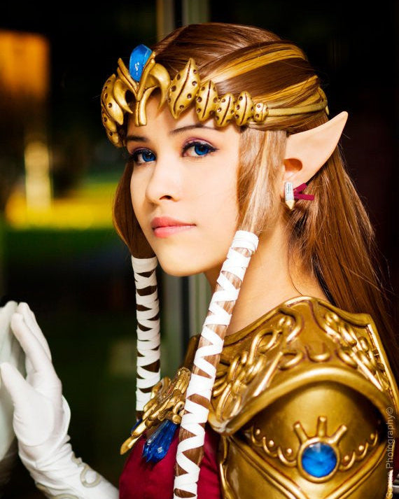 A person wearing a costume featuring anime-style elf ears, with gold-colored headpiece and armor.